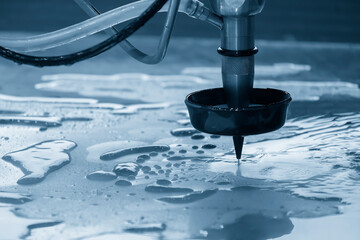 The abrasive waterjet cutting machine cutting the metal plate in the light blue scene.