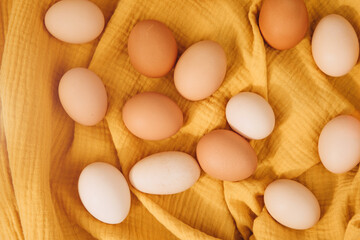 Chicken eggs of different brown and beige shades on a yellow textile background. Easter background. Top view