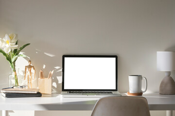 Front view laptop with blank screen, houseplant, coffee cup and office supplies on white table.