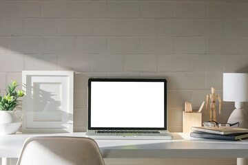 Computer laptop with blank screen, houseplant and coffee cup on white table with brick wall.