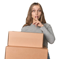 Blonde woman with cardboard boxes moving on studio backdrop keeping a secret or asking for silence.