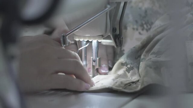 This stock video shows the hands of a seamstress who sews trousers made of camouflage fabric for the military on a sewing machine. This video will decorate your projects related to seamstresses.