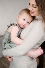 Young mother holds a one-year-old barefoot child in her arms. Concept of care, love, affection, motherhood.Vertical.