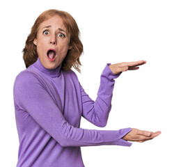 Redhead mid-aged Caucasian woman in studio shocked and amazed holding a copy space between hands.