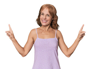 Redhead mid-aged Caucasian woman in studio indicates with both fore fingers up showing a blank...