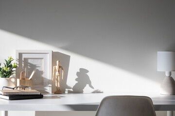 Comfortable workplace with picture frame, coffee, stationery and houseplant on white table. - obrazy, fototapety, plakaty