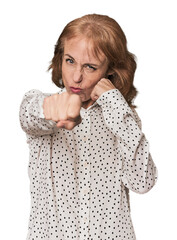 Redhead mid-aged Caucasian woman in studio throwing a punch, anger, fighting due to an argument,...