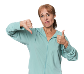 Young mid-aged woman in sportswear in studio showing thumbs up and thumbs down, difficult choose concept