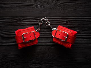 red handcuffs over black wooden backdrop. bdsm background
