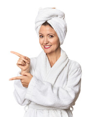 Caucasian woman in bathrobe and towel excited pointing with forefingers away.