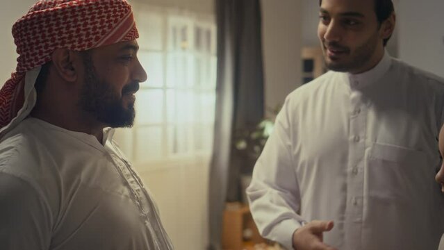 Side chest up footage of cheerful bearded uncle or family friend excitedly talking to little boy and to his father gathered together to celebrate islamic holiday Eid al-Fitr at home