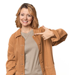 Blonde middle-aged Caucasian woman in studio person pointing by hand to a shirt copy space, proud...