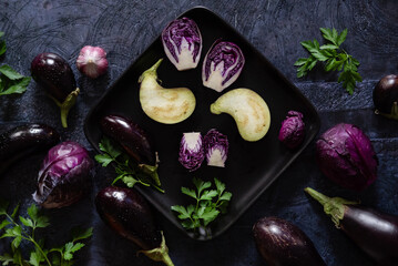 Assortment raw organic of purple vegetables mini eggplants, spring onion, beetroot, radicchio salad, plums, kohlrabi, flower salt over dark metal background. Top view with space. Food frame