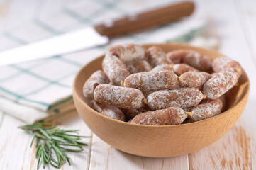 Pork fermented dry cured mini sausages in a bowl on a white wooden table.