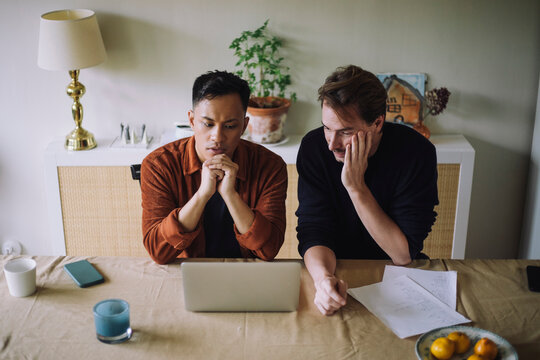 High angle view of worried gay couple sitting with laptop on table at home