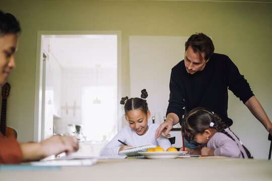 Father homeschooling daughters sitting at dining table
