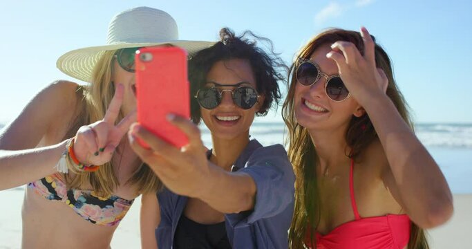 Friends, women and laughing on beach with selfie for social media update, profile picture and internet post on holiday. Group, people and bonding with sunglasses by ocean with peace sign or happiness