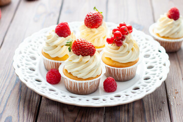 Vanilla cupcakes decorated with fresh strawberry, raspberry and red currant on rustic wooden background