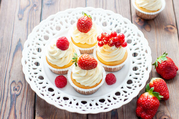 Vanilla cupcakes decorated with fresh strawberry, raspberry and red currant on rustic wooden background