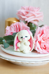 Cute bunny toy made of white chocolate with fresh pink peonies on the background