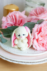 Cute bunny toy made of white chocolate with fresh pink peonies on the background