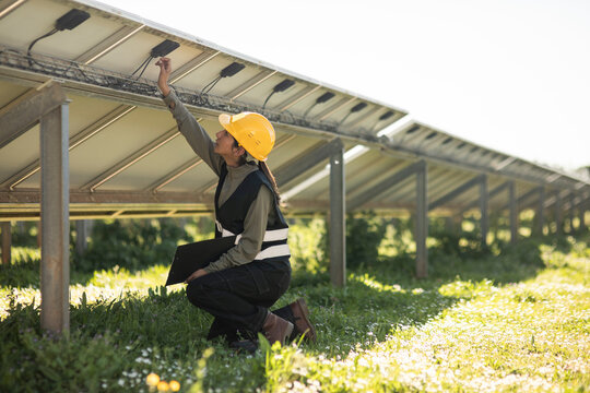 Female engineer fixing connection of solar panels while kneeling at power station