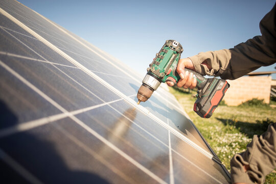 Hand of female engineer installing solar panels with drill while working at power station