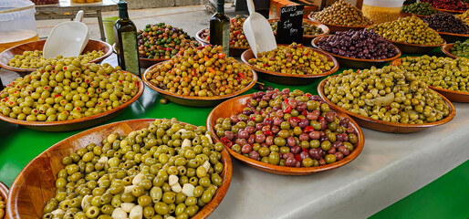 Shot showing a varied display of many types of fresh and dressed olives in wooden bowls, for sale...