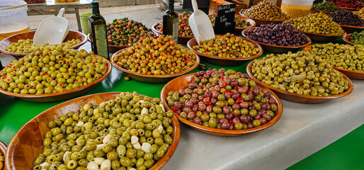 Shot showing a varied display of many types of fresh and dressed olives in wooden bowls, for sale at a supermarket or market