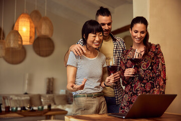 Smiling friends talking to someone over the video call, drinking wine, smiling.