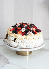 Pavlova cake with whipped cream cheese, chocolate sauce and fresh berries on grey background