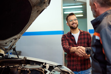 A male customer is doing a handshake with a mechanic at the garage. - 750726854