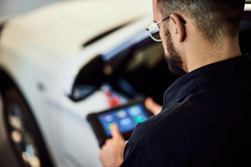 A mechanic man doing a diagnostic of the car, using a digital tablet.