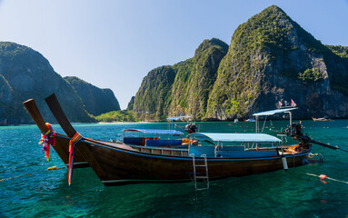 View of Maya bay with limestone rocks, white beach and blue clear water with long tail boats mooring in front of Bay. Phi-Phi Islands, Krabi, Thailand.