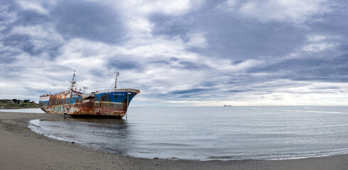 Rusted Shipwreck on Serene Beach Under Cloudy Sky