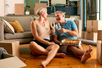 Mature Couple Celebrating In New Home On Moving Day Eating Pizza And Drinking Wine - 750730290
