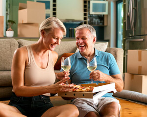 Mature Couple Celebrating In New Home On Moving Day Eating Pizza And Drinking Wine - 750730839