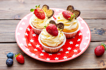 Set of vanilla cupcakes decorated with fresh strawberries, blueberries, chocolate hearts and golden sprinkles on red star plate