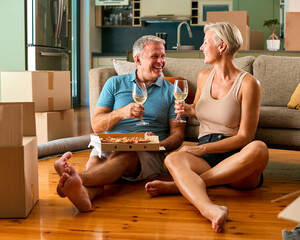 Mature Couple Celebrating In New Home On Moving Day Eating Pizza And Drinking Wine