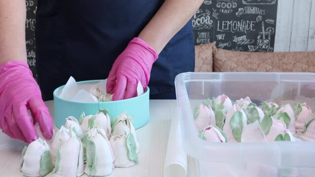 A woman puts a homemade marshmallow in a box.  The box is turquoise in color. There are zephyr tulips on the table next to it.