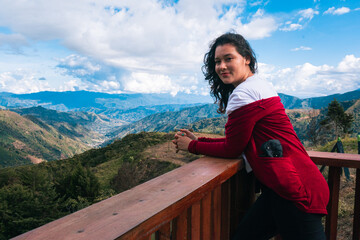 Fototapeta na wymiar Hermosa mujer usando abrigo rojo posa para con hermoso paisaje de fondo de montañas y cielo azul