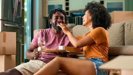 Young Couple Celebrating In New Home On Moving Day Eating Pizza And Drinking Wine - 750735491