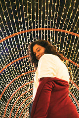 Joven mujer hermosa posa con luces navideñas de fondo