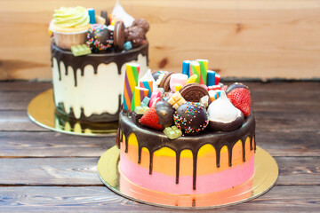 Two bright colorful richly decorated cakes with sweets, popsicles, lollipops, jelly, strawberries and cupcakes on rustic background