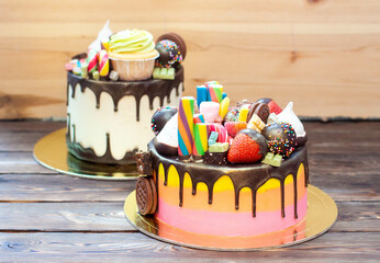 Two bright colorful richly decorated cakes with sweets, popsicles, lollipops, jelly, strawberries and cupcakes on rustic background