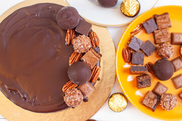 Decoration of chocolate cake with chocolate balls, truffles, pecan nuts, pieces of brownie and toffees, flat lay