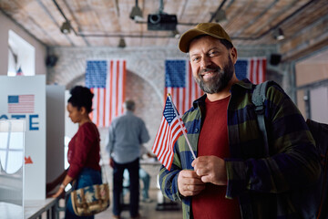 Happy mature man with USA flag at polling place looking at camera.
