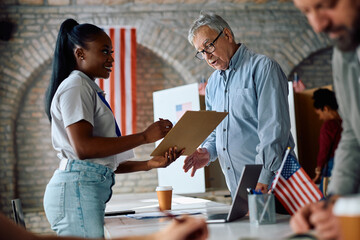 Happy black volunteer assisting senior citizen for signing up to vote during US elections.