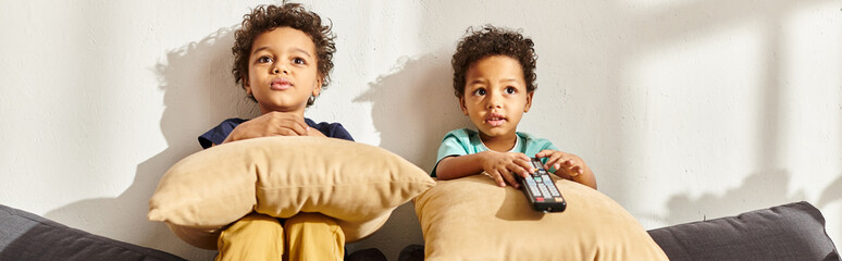 adorable african american boys sitting on sofa with pillows and watching interesting movies