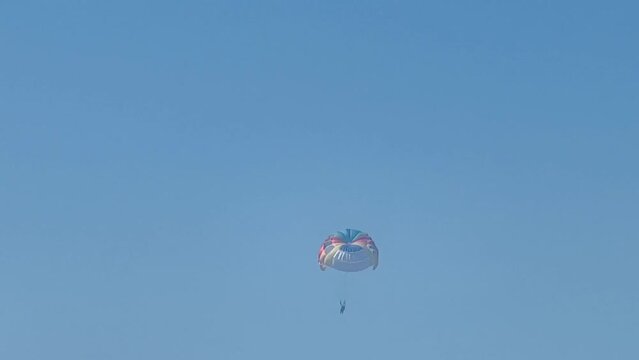 Parasailing above the sea, colourful parachute soaring in clear blue sky